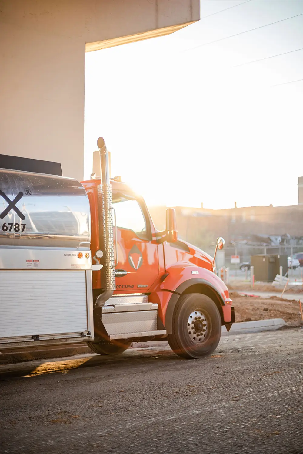 A red FuelFox tanker truck parked at a job site, backlit by the setting sun.
