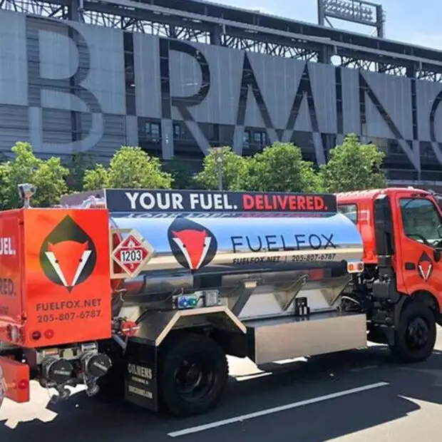An orange and silver FuelFox tanker truck parked outside a stadium with a large "Birmingham" sign in the background.