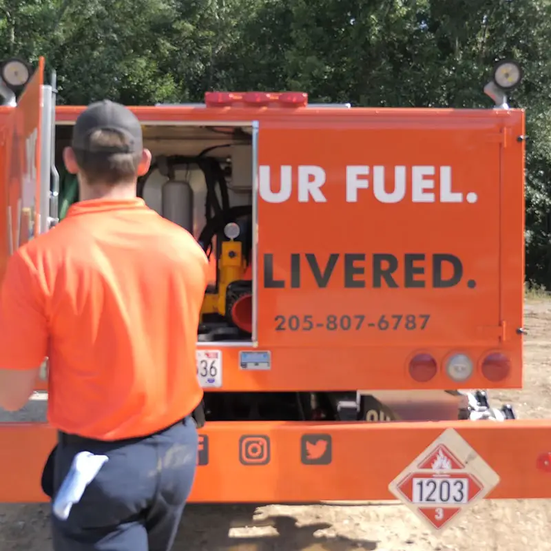 A FuelFox driver in an orange uniform opening the truck's rear equipment compartment.