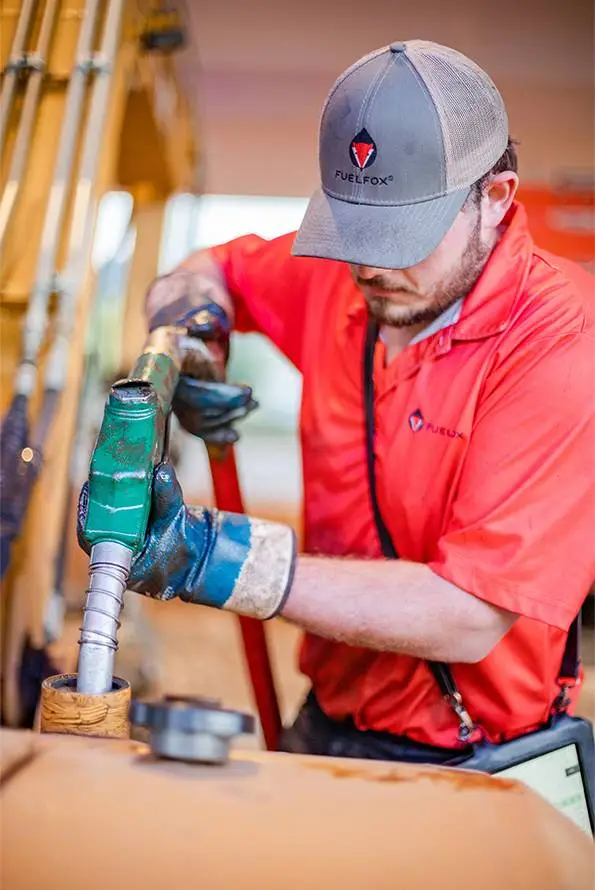 A FuelFox driver in a red uniform and FuelFox cap fueling a piece of equipment.